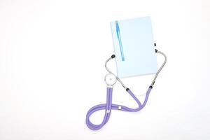 A lilac phonendoscope lies on a table with a notepad and a pen, view from above photo