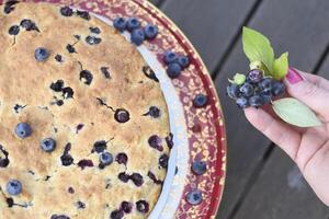 un mujer mano decora un Fresco tarta con arándanos, tronar a comida casera foto