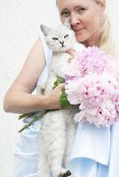 el anfitriona abrazos un linda gris gatito con verde ojos de el escocés, azul vestir foto