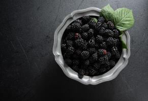 A full plate of the ripe blackberries,a sprig of red berries on a pewter bowl photo