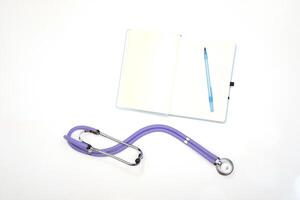 A lilac phonendoscope lies on a table with a notepad and a pen, view from above photo