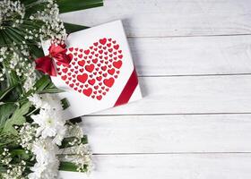 Valentine's day gift, red heart praline box and flower bouquet on white table photo