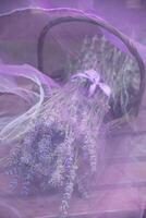 lavender bouquet in a wicker basket under transparent purple chiffon on a wooden photo