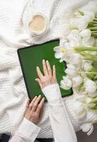 verde pantalla tableta, joven mujer mirando para de la madre día regalo en línea, tulipanes foto