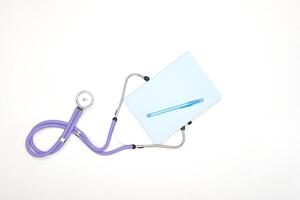 A lilac phonendoscope lies on a table with a notepad and a pen, view from above photo