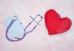 notepad and pen phonendoscope, toy red heart on the table top view, medical photo