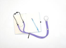 A lilac phonendoscope lies on a table with a notepad and a pen, view from above photo