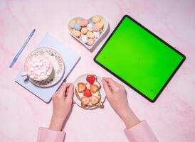 woman holding soft cheese and strawberry sandwich near green screen tablet photo