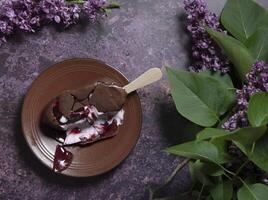 melted raspberry ice cream in chocolate on a wooden stick on a dark table photo