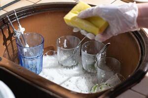 woman washing dishes in the sink with gloves with detergent photo