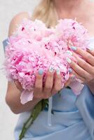 irreconocible niña en un azul vestir con un ramo de flores de rosado peonías demuestra un original uña diseño con azul color foto