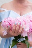 novia en un azul Boda vestir con un ramo de flores de rosado peonias, pastel paraíso foto