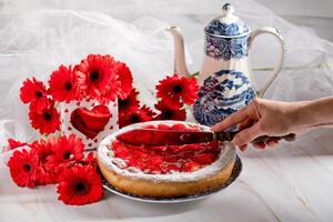 todavía vida, un mujer cortes un fresa tarta en un mesa decorado con rojo gerberas foto