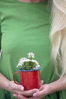 a blonde girl with long hair in a bright green dress holding a red mug photo