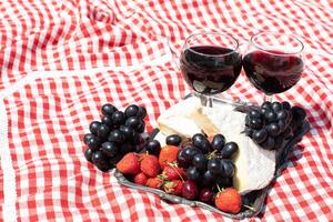 verano picnic en un verde césped con rojo vino, queso y Fresco bayas, uvas foto