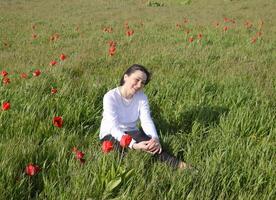 Beautiful fairy young girl in a field among the flowers of tulips. Portrait of a girl on a background of red flowers and a green field. Field of tulips photo