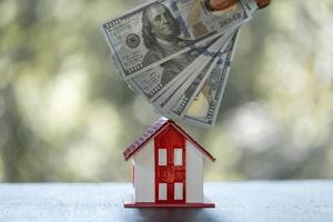 Model of house with dollar bill on table on blurred background. Money saving or investing for home loan or real estate. Investment property, Saving money for retirement concept. photo