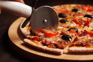Cutting ham pizza on wooden board close up photo