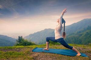 Woman doing yoga asana Virabhadrasana 1 - Warrior pose outdoors photo