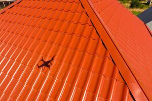 House with an orange roof made of metal, top view. Metallic profile painted corrugated on the roof. photo