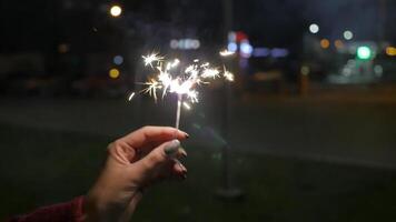 vicino su di donna Tenere sparkler su il strada. avvicinamento di ragazza con spumanti. femmina mano Tenere sparklers nel il strada. vacanza concetto video