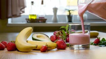 fraise banane smoothie est versé dans une verre sur le Contexte de Frais des fruits. Milk-shake est prêt à boire. le concept de en bonne santé et végétarien nourriture video