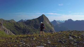 Aerial view of girl with a backpack goes on a mountain ridge. Beautiful view of the peaked tops of the Lofoten Islands. Norway 4k video