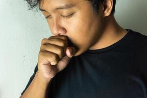 man feeling ill with a sore throat. Cold symptoms. Close up of asian man coughing. photo