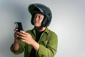 adulto asiático hombre confuso cuando mirando a su teléfono de mano mientras vistiendo motocicleta casco foto