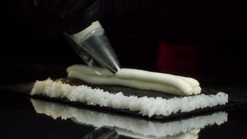 Close-up view of process of preparing roll sushi. Chef in gloves imposes from pastry bag of cream filling on sheet of nori with rice. Art of making sushi rolls video