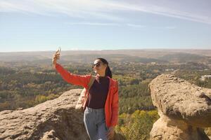 joven hermosa mujer viajero tomando selfie retrato en montaña parte superior - contento sonriente niña utilizando teléfono inteligente - excursionismo y alpinismo rock foto