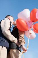 cheerful romantic couple dating and kissing outdoors with balloons photo