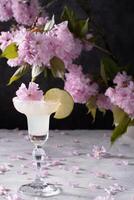 Spring still life with a glass of cold Margarita with lime, pink sakura flowers photo