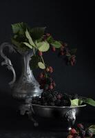 A full plate of the ripe blackberries,a sprig of red berries on a pewter bowl photo