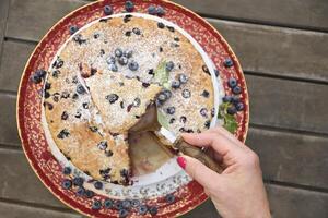 a woman's hand holds a piece of blueberry pie, a summer sweet dessert photo