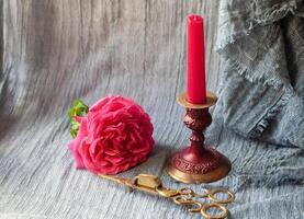 red candle in burgundy copper candlestick with brass scissor fire extinguisher and pink rose as a Valentines Day gift photo
