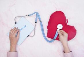 notepad and pen phonendoscope, toy red heart on the table top view, medical photo