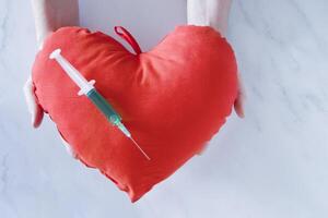 syringe with green liquid on soft red heart concept of vaccination or treatment photo
