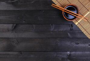 Bamboo mat, soy sauce, chopsticks on dark table photo