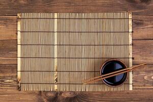 Mat for sushi and chopsticks on wooden background. Top view with copy space photo