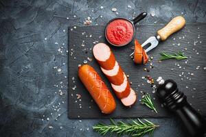 Grill pork sausages on a black stone slate serving board, isolated on a dark background. photo