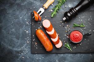 Grill pork sausages on a black stone slate serving board, isolated on a dark background. photo