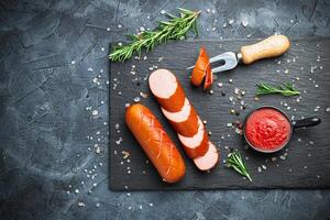 Grill pork sausages on a black stone slate serving board, isolated on a dark background. photo