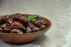 Dates in a brown plate on a textured light background, side view photo