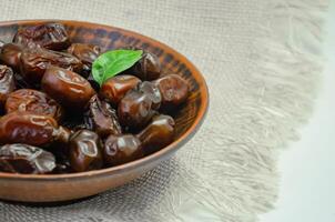 Dates in a brown plate on a textured light background, side view photo