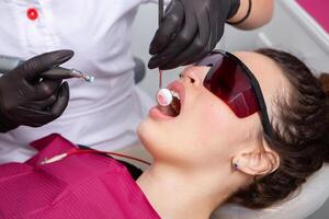 Closeup of female patient showing her beautiful white teeth while having treatment at dental clinic, dentist hands in rubber gloves holding dental tools photo