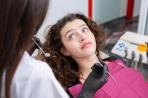 de cerca de hembra paciente demostración su hermosa blanco dientes mientras teniendo tratamiento a dental clínica, dentista manos en caucho guantes participación dental herramientas foto