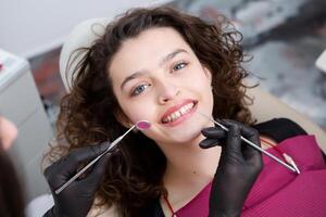 Portrait of young smiling woman sitting in stomatology clinic chair and doctor's hands with dental Mouth mirror and Dental explorer tools preparing to examine teeth condition. photo