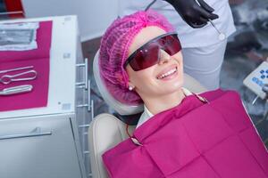 Portrait of young smiling woman sitting in stomatology clinic chair and doctor's hands with dental Mouth mirror and Dental explorer tools preparing to examine teeth condition. photo