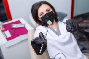 Dentist examining patient teeth in dental clinic. Dentistry and healthcare. Dentist holding dental tools in her hands. photo